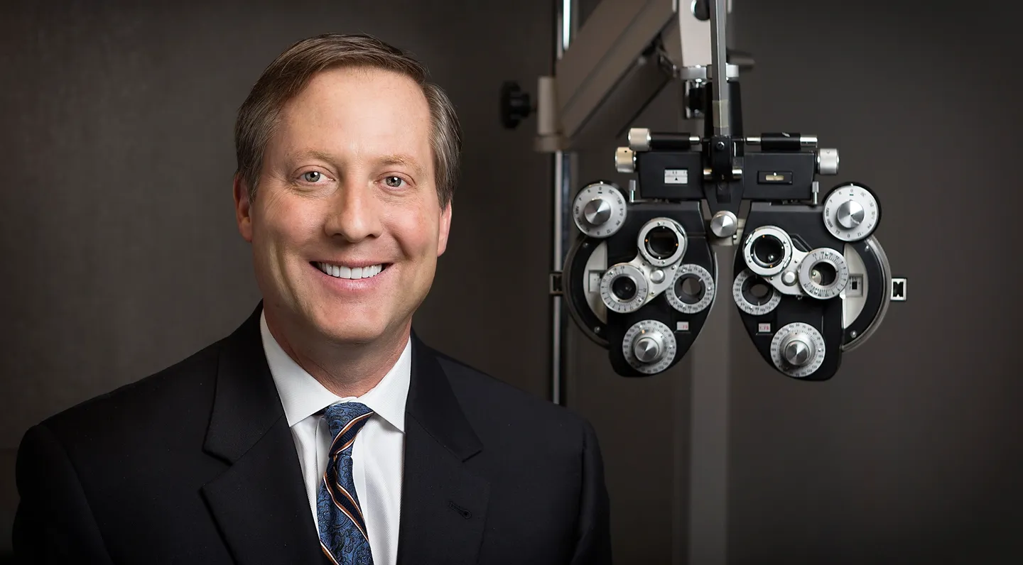 A man in suit and tie standing next to an eye exam machine.